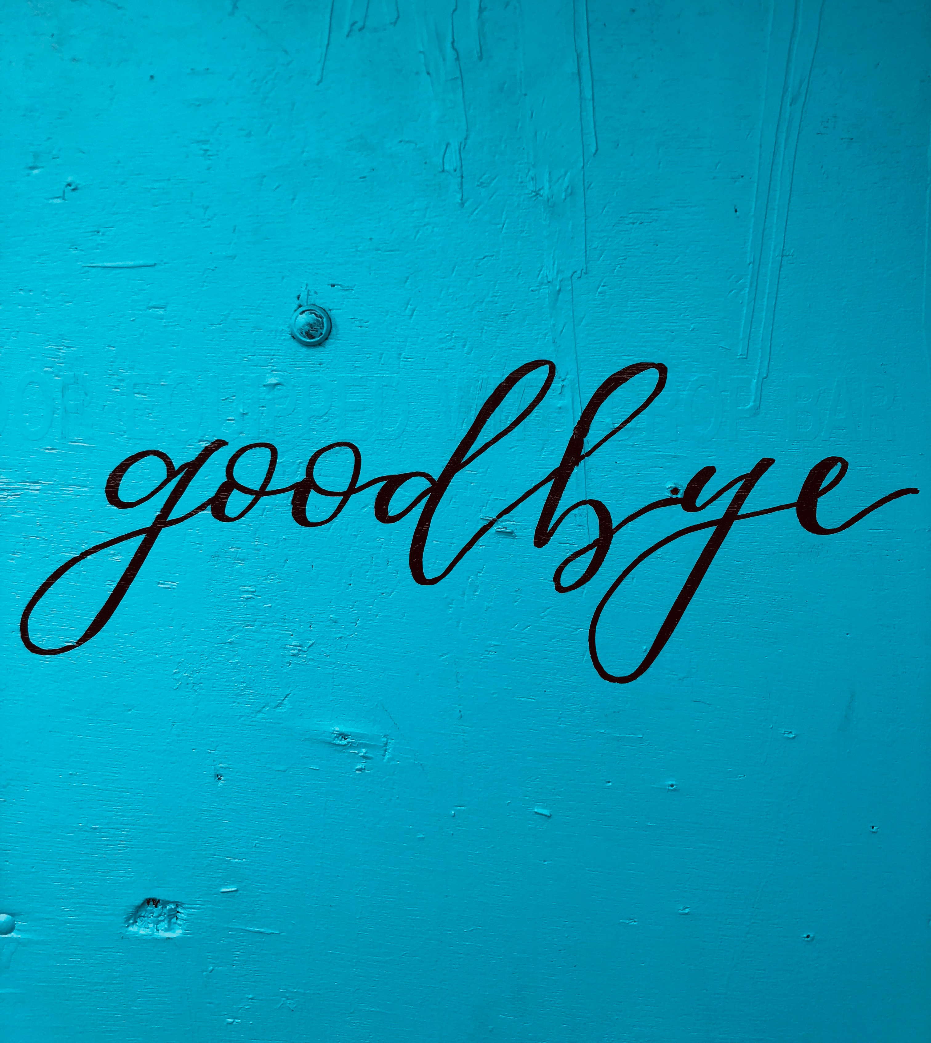 A teal wood panel with the word, "goodbye," painted on it.
